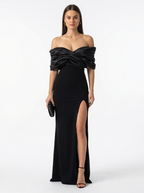 Woman wearing a black off-shoulder gown with a high slit on a white background