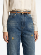 Person wearing blue jeans with a white shirt on a plain background