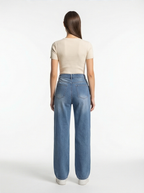 Person wearing blue jeans and a beige top on a white background