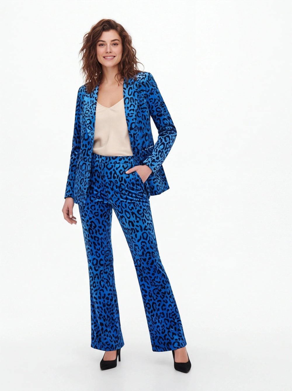 A woman modeling a blue and black leopard-print pantsuit, consisting of a blazer and matching wide-leg trousers, styled with a beige camisole and black heels against a white studio background.