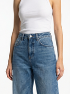 Person wearing blue jeans and a white tank top on a plain background