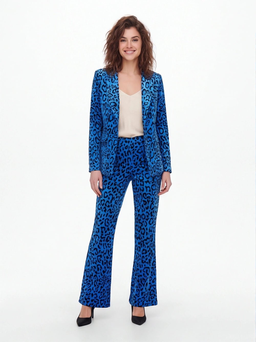 A woman modeling a blue leopard-print pantsuit with a blazer and matching wide-leg trousers, styled with a cream camisole top and black heels against a plain white studio background.