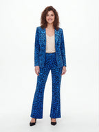 A woman modeling a blue leopard-print pantsuit with a blazer and matching wide-leg trousers, styled with a cream camisole top and black heels against a plain white studio background.
