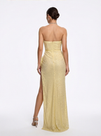 Woman wearing a strapless yellow evening gown with a slit on a white background