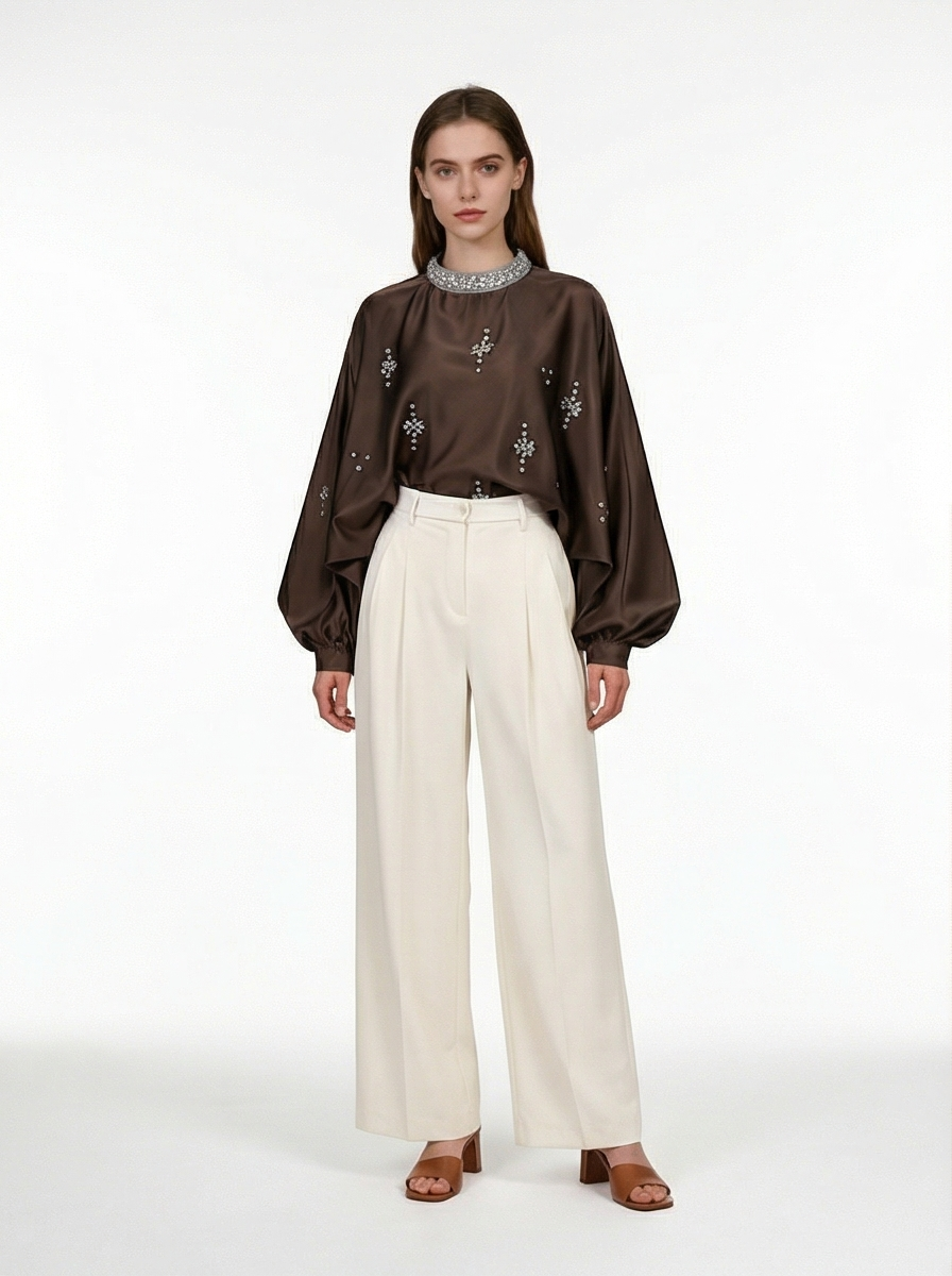 Woman wearing a brown blouse with floral patterns and white pants on a white background