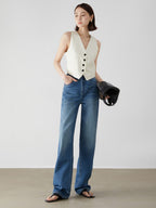 Woman wearing a white sleeveless vest and blue jeans against a plain background