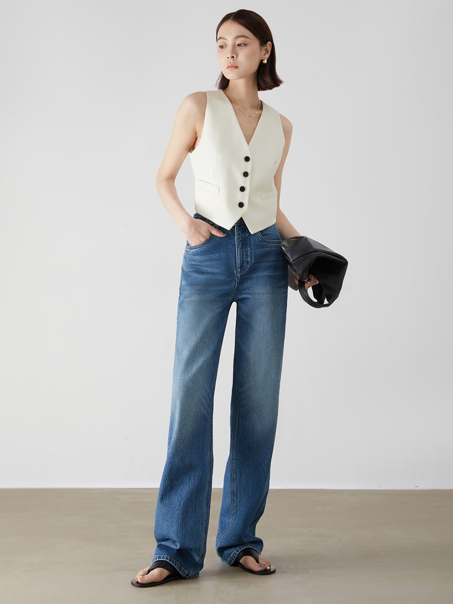 Woman wearing a white sleeveless vest and blue jeans against a plain background