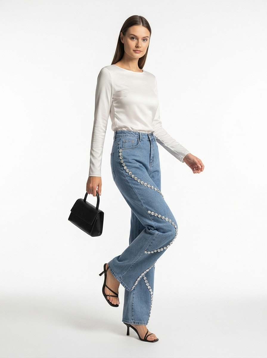 Woman wearing a white long-sleeve top and blue jeans with embellishments on a white background