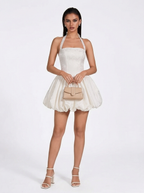 Woman wearing a white dress with a beige handbag on a white background