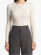 Person wearing a beige ribbed sweater and gray pleated pants on a white background
