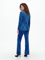 A woman modeling a blue and black leopard-print velvet pantsuit, shown from a rear three-quarter angle against a plain white studio background.