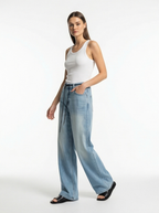 Woman wearing a white tank top and light blue jeans on a white background