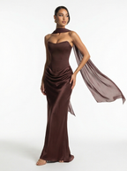 Woman wearing a brown strapless gown with a flowing fabric on a white background