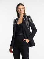 Woman wearing a black blazer with white embellishments on a white background