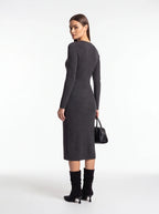 A woman modeling a dark gray long-sleeve midi dress from the back, paired with black knee-high boots and holding a small black handbag, against a plain white studio background.