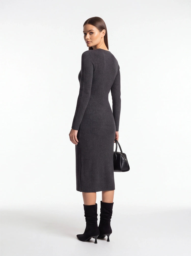 A woman modeling a dark gray long-sleeve midi dress from the back, paired with black knee-high boots and holding a small black handbag, against a plain white studio background.
