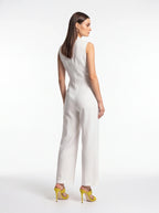 A woman modeling a white sleeveless wide-leg jumpsuit from the back, paired with bright yellow high-heeled sandals, against a plain white studio background.