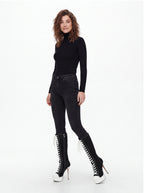 A woman modeling a black long-sleeve mock neck top, black skinny jeans, and black lace-up knee-high boots with white platform soles, photographed against a plain white studio background.