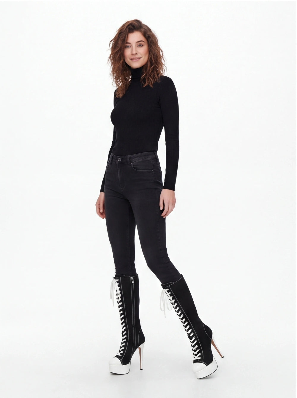 A woman modeling a black long-sleeve mock neck top, black skinny jeans, and black lace-up knee-high boots with white platform soles, photographed against a plain white studio background.