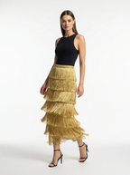 Woman wearing a black top and gold fringed skirt on a white background