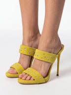 Yellow open-toe high-heel sandals with studded ankle straps, shown on a model's feet against a white studio background.