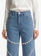 Blue jeans with decorative chain details worn by a person on a white background