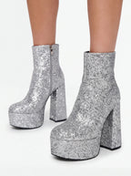 Silver glitter platform ankle boots with chunky block heels, shown on a model's feet against a white background.