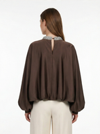 Woman wearing a brown blouse with a cut-out back design on a white background
