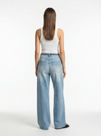 Woman wearing light blue jeans and a white tank top on a white background