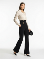 Woman wearing a white blouse and black high-waisted pants with gold buttons on a white background