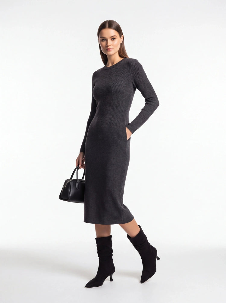A woman modeling a dark gray long-sleeve knit midi dress with side pockets, paired with black ankle boots and a black handbag, against a plain white studio background.