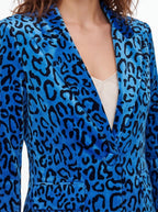 A close-up of a model wearing a vibrant blue velvet blazer with a black leopard print pattern, layered over a light beige top.
