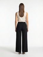 Woman wearing a white sleeveless top and black wide-leg pants on a white background